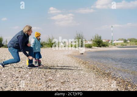 Vater und Tochter schauten auf den Fluss, während sie Kiesel hinein warfen Wasser in der Nähe des Flussufers Stockfoto