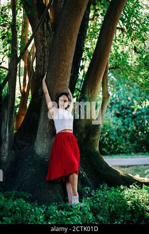 Junge Frau mit aufgehobenen Armen, die im Park bei einem Baum stehen Stockfoto