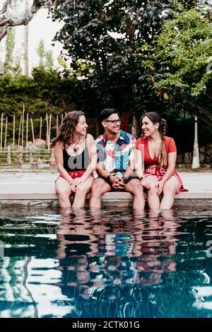 Lächelnde Freunde reden, während sie am Pool sitzen Stockfoto