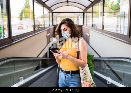 Junge Frau SMS-Nachrichten während des Stehens mit Netztasche auf Laufsteg an der U-Bahn Stockfoto