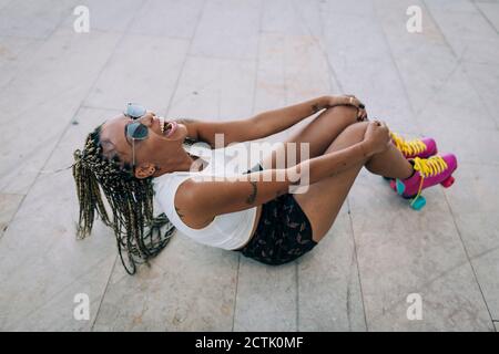 Frau mit Rollschuhe lachen, während sie auf dem Fußweg sitzt Stadt Stockfoto