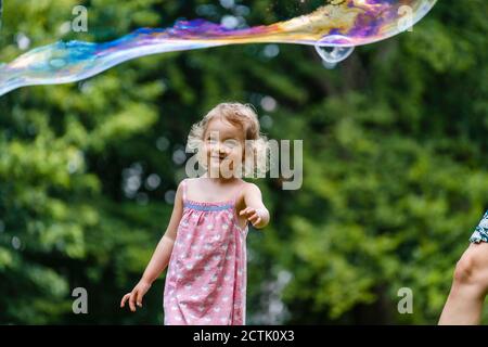 Lächelndes Mädchen, das auf Blase schaut, während es im Park steht Stockfoto