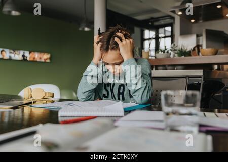 Schuljunge zu Hause lernen, Kopf in den Händen, Problem zu lösen Stockfoto