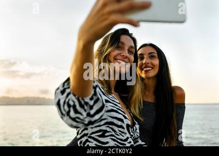 Freunde lächeln, während sie Selfie gegen klaren Himmel machen Stockfoto