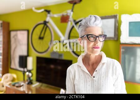 Ältere Frau schaut weg, während sie zu Hause steht Stockfoto