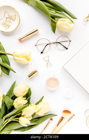 Weiblicher Arbeitsplatz mit gelben Tulpenblüten, Damenmode goldene Accessoires, Tagebuch, Gläser auf weißem Hintergrund. Flach liegend. Draufsicht Hintergrund. Stockfoto