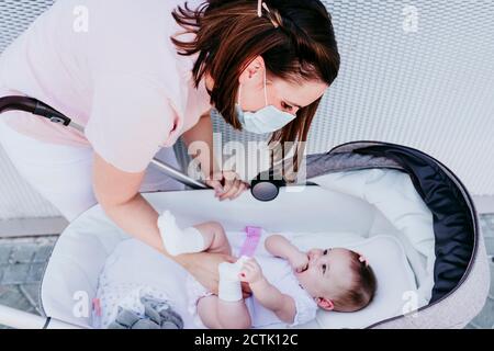 Mutter trägt Schutzmaske, Kuscheln Baby Mädchen im Kinderwagen Stockfoto