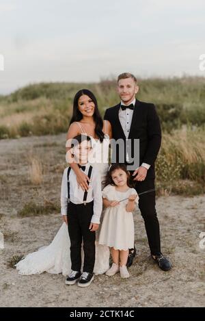 Lächelnde Eltern mit Kindern tragen Hochzeitskleid, während sie im Stehen Ein Stockfoto
