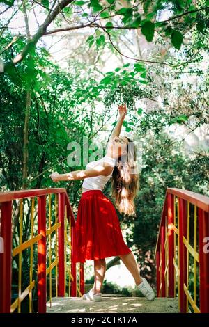 Junge Frau übt Ballett auf Fußgängerbrücke gegen Bäume im Park Stockfoto