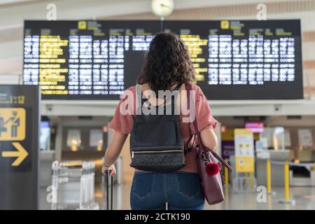 Junge Frau, die ihren Flug an der Zeittafel am Flughafen überprüft Stockfoto