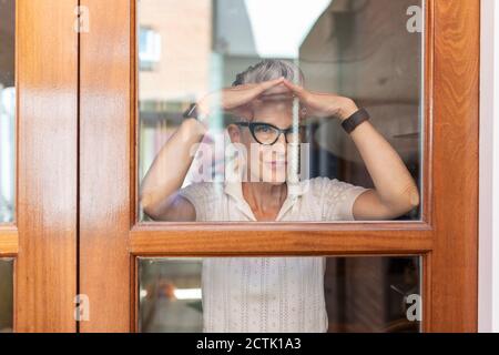 Ältere Frau, die Handbewegung macht, während sie aus dem Fenster schaut Zu Hause Stockfoto