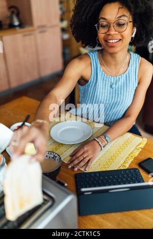 Junge Frau mit digitalem Tablet auf dem Tisch beim Frühstück Zu Hause Stockfoto