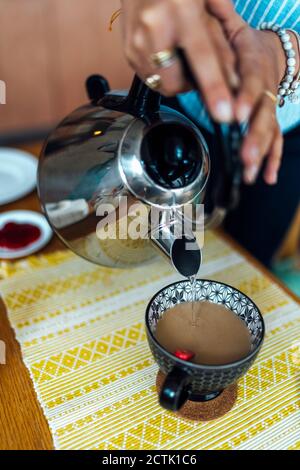 Nahaufnahme einer jungen Frau, die Wasser in die Kaffeetasse gießt Tisch zu Hause Stockfoto