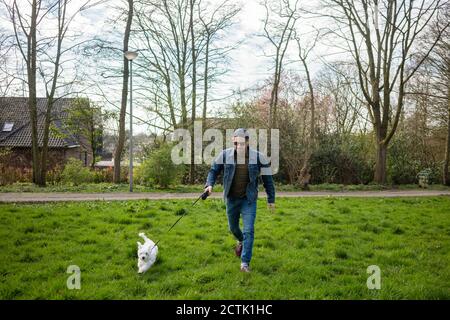 Lächelnder Mann läuft mit Hund auf Gras im Hof Stockfoto