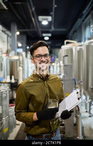 Portrait von glücklichen Mann hält Zwischenablage und Bierglas in Handwerkliche Brauerei Stockfoto