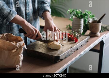 Hände von Mann schneiden frisches hausgemachtes Brot an Bord in Küche Stockfoto