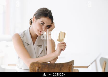Junge Frau mit Visitenkarte, während sie auf einem Stuhl sitzt Büro Stockfoto