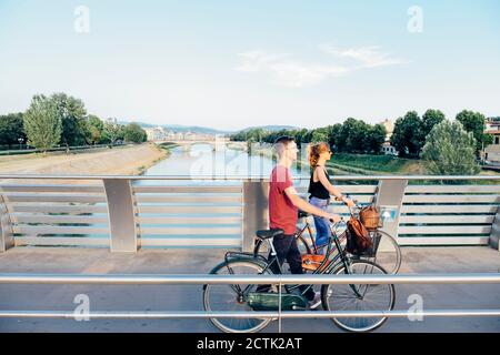 Paar mit Fahrrädern, die auf der Brücke über den Fluss gegen den Himmel laufen Stockfoto