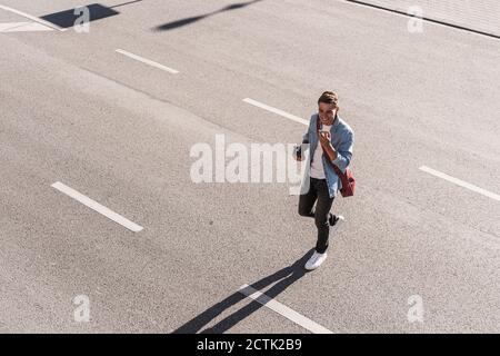 Lächelnder Mann, der auf dem Handy telefoniert, während er die Straße überquert Stadt Stockfoto
