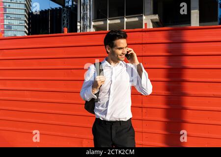 Der Pendler spricht über das Mobiltelefon, während er gegen die Wand steht In der Stadt Stockfoto