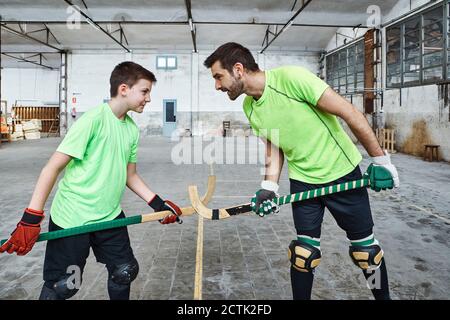 Vater und Sohn halten Hockeyschläger, während sie Gesicht zu stehen Gesicht beim Spielen auf dem Platz Stockfoto