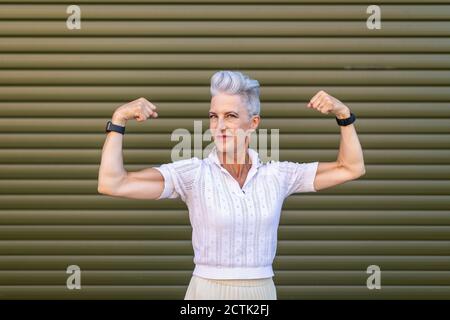 Ältere Frau, die Muskeln beugend, während sie gegen den Verschluss steht Stockfoto