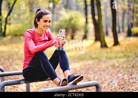 Junge Joggerin mit smartphoneon sitzt auf Fahrrad stehen in Herbstwald Stockfoto