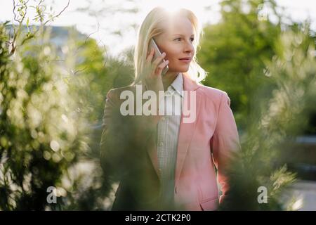 Durchdachte Geschäftsfrau, die wegschaut, während sie mit dem Mobiltelefon spricht Stadt Stockfoto