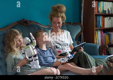Lächelnde Frau, die Kinder ansieht, die mit Robotern spielen, die darauf sitzen Sofa im Wohnzimmer zu Hause Stockfoto