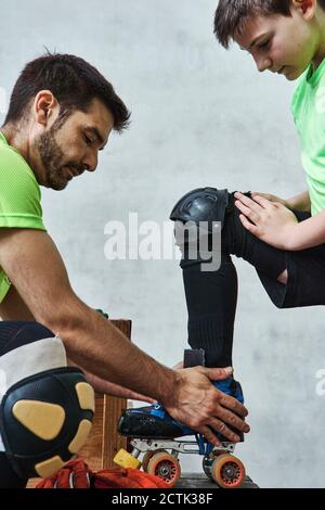 Mann hilft Sohn trägt Rollschuh vor dem Training Stockfoto