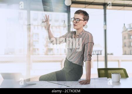 Geschäftsfrau, die im Büro auf dem Schreibtisch sitzt und die Hand hebt Stockfoto