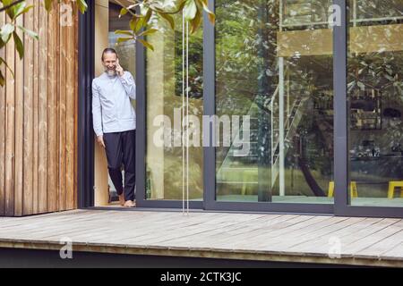 Reifer Mann, der über Smartphone spricht, während er am Eingang steht Von in winzigen Haus Stockfoto