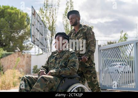 Serious Armee Soldat hilft einem anderen Militäroffizier auf Rollstuhl sitzen Stockfoto