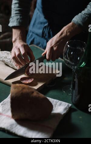 Mittelteil des Mannes, der Salami an Bord am Tisch schneidet Stockfoto