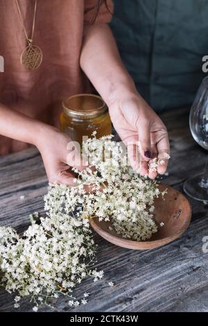 Mittelteil der Frau bereitet frischen Cocktail mit weißen Blumen auf Holztisch Stockfoto