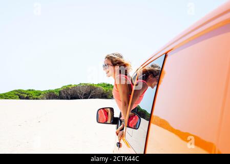 Frau mit wehenden Haaren, die sich durch das Fenster aus dem Auto lehnte Stockfoto