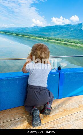 Kleiner Junge, der vor dem Geländer kniet und den malerischen Blick auf den Kerkini-See, Mazedonien, Griechenland, betrachtet Stockfoto