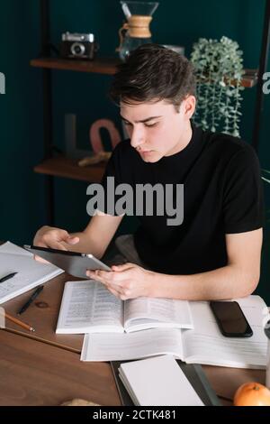 Schöner Mann mit digitalen Tablet beim Sitzen am Tisch tun Hausaufgaben Stockfoto