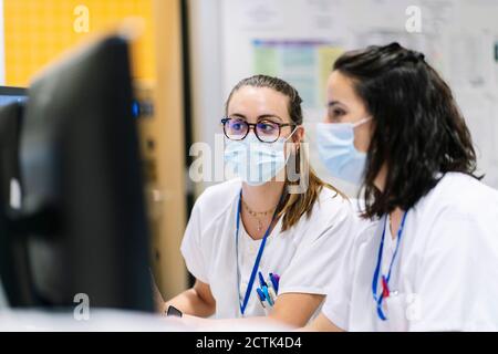 Nahaufnahme von Ärztinnen, die Masken tragen, mit Computern im Krankenhaus Stockfoto