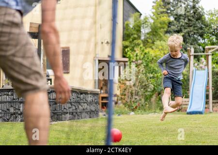 Blonde Junge tritt Ball beim Fußballspielen mit Vater an Hinterhof Stockfoto