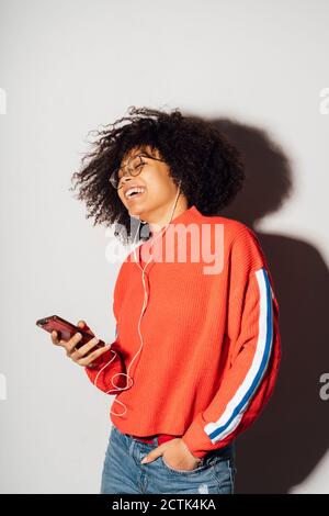 Glückliche Frau, die im Stehen Musik auf dem Smartphone hört Vor weißem Hintergrund Stockfoto