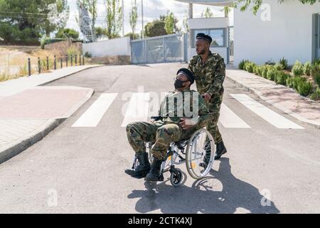 Armeeoffizier hilft einem anderen Soldaten im Rollstuhl sitzen Stockfoto