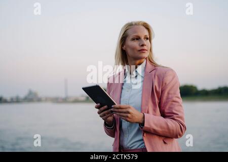 Nachdenkliche weibliche Unternehmerin, die wegschaut, während sie digitale Tablette gegen hält Himmel Stockfoto