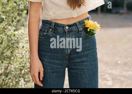 Frau steht mit gelber Blume in der Tasche Stockfoto