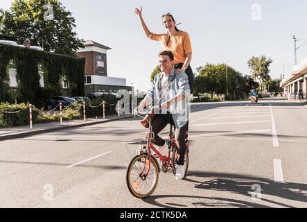 Fröhliche junge Frau hinter Freund Fahrrad auf der Straße Stockfoto