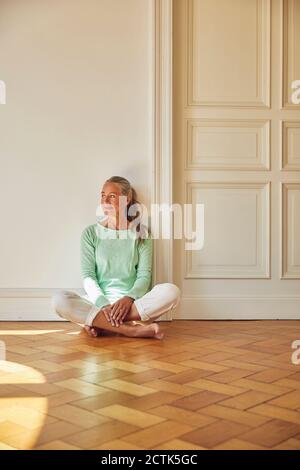 Nachdenkliche Frau, die zu Hause auf dem Boden an der Tür sitzt Stockfoto