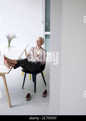 Lächelnde Geschäftsfrau mit den Füßen nach oben auf einem Stuhl im Loft entspannen Büro Stockfoto