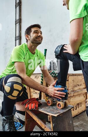 Lächelnder Mann, der den Sohn ansieht, während er beim Tragen von Skaten hilft Stockfoto