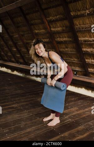 Lachende Frau rollt Yogamatte auf Stockfoto