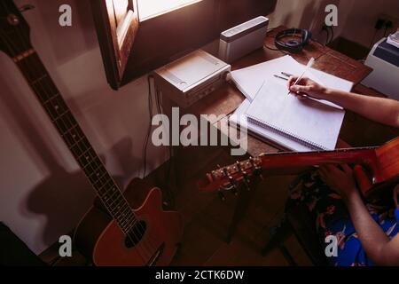 Junge Frau, die im Buch schreibt, während sie Gitarre im Leben übt Zimmer Stockfoto